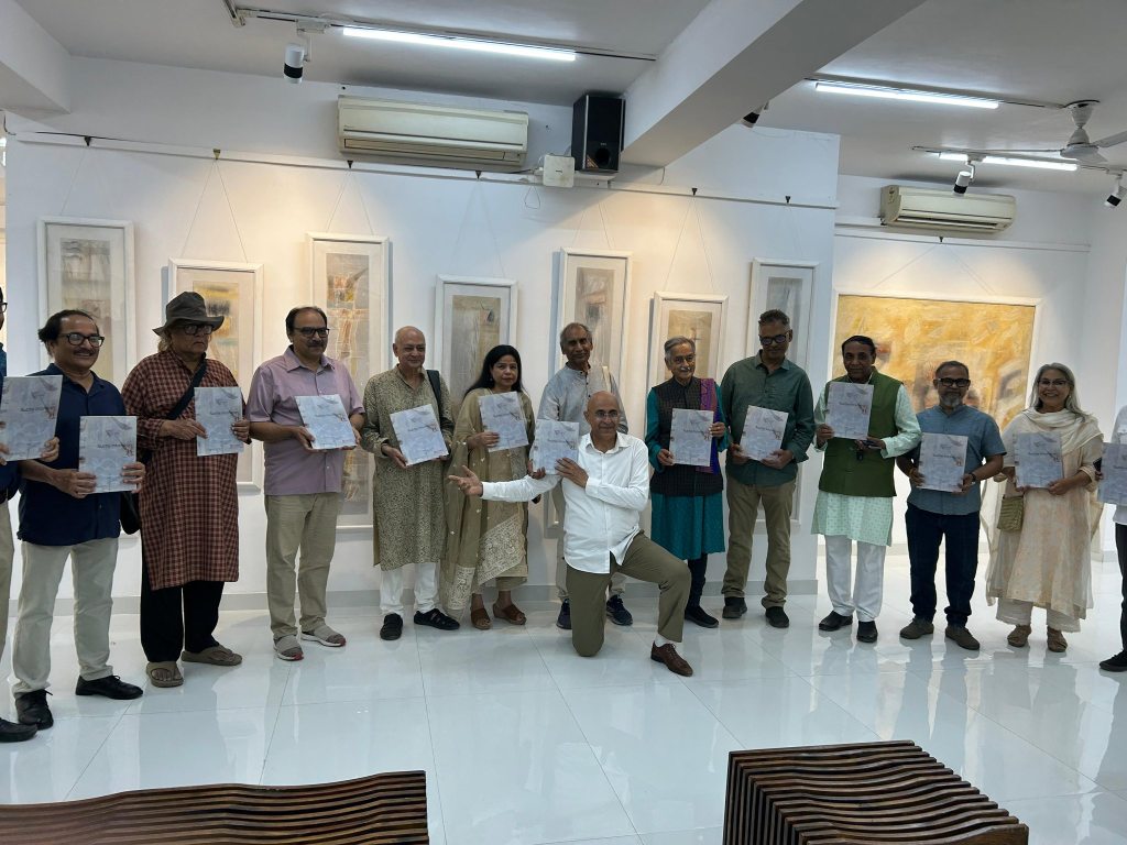 A group of individuals posing together in an art gallery, holding art-related documents or brochures. The setting features white walls with framed artwork displayed in the background.