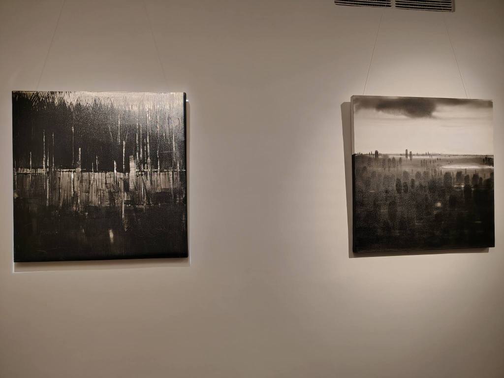 Two black and white abstract paintings hanging on a gallery wall, featuring vertical lines and blurred landscapes.