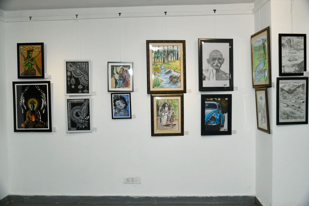 A collection of framed artwork displayed on a white wall, featuring various styles including religious themes, portraits, and landscapes.