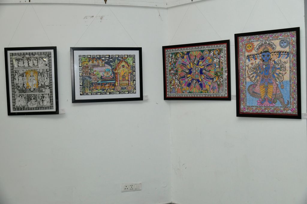 A gallery display featuring four framed artworks on a white wall, showcasing intricate paintings with religious and cultural themes.