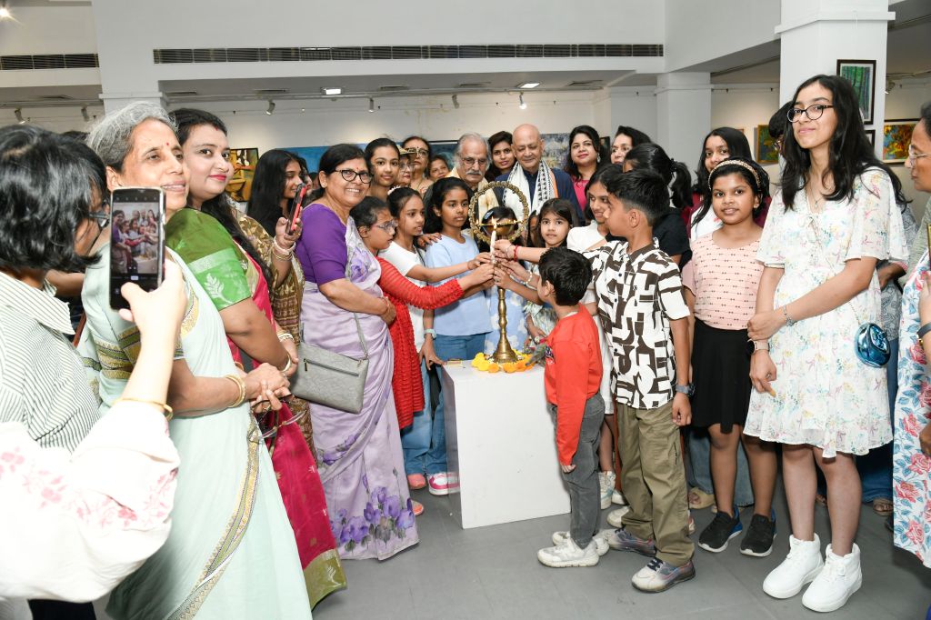 A diverse group of adults and children participating in a cultural event, gathered around a decorative lamp that is being lit, in an art gallery setting.