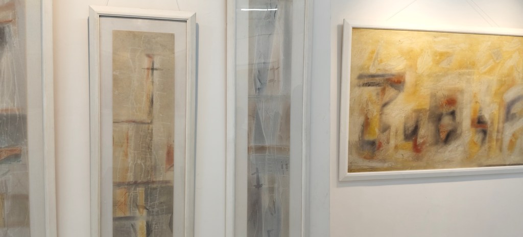 Two abstract paintings framed and displayed on a white wall, featuring a mix of muted colors and geometric shapes.