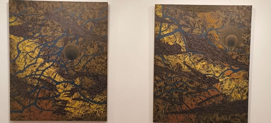 Two abstract artworks displayed on a wall, featuring intricate patterns in gold, black, and blue, with dark circular elements at the center.