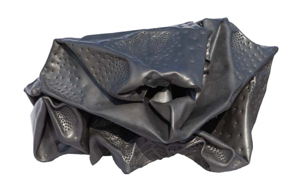 A sculptural piece made of dark, crumpled material featuring textured surfaces with perforations.
