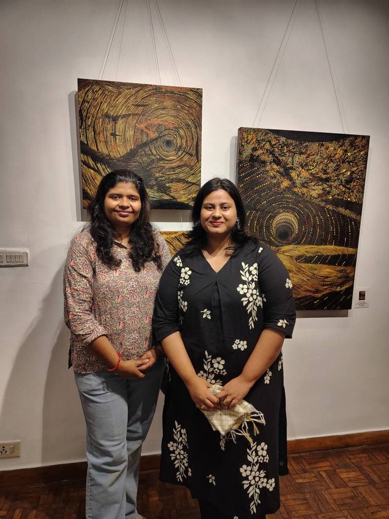 Two women posing together in front of art pieces on display in a gallery.