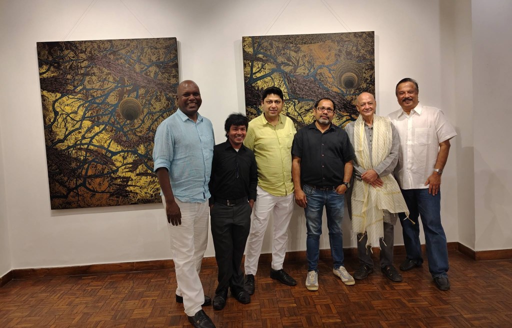 A group of six individuals posing for a photo in an art gallery, with colorful abstract paintings hanging on the walls behind them.