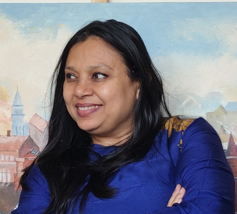 A woman with long black hair smiling while standing in front of a colorful, painted background depicting houses and a skyline.